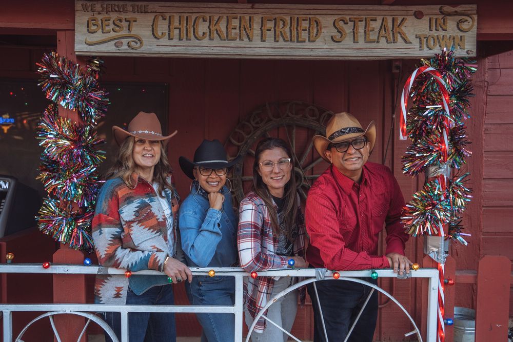A group of people pose on a red porch decorated with holiday garland and festive Christmas decorations.