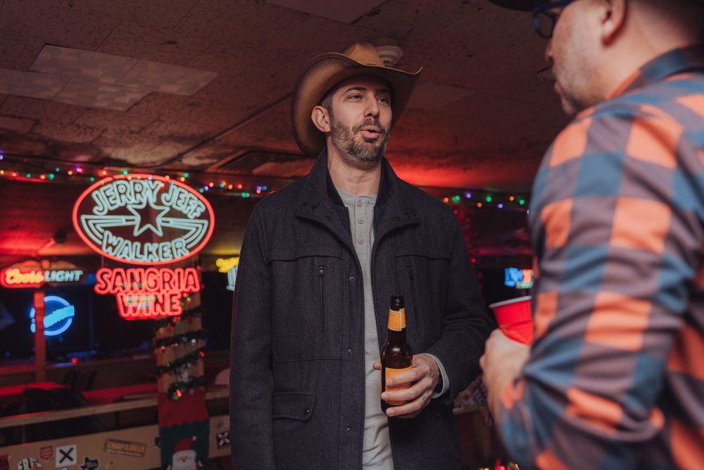 People socialize in a dimly lit bar with neon signs and string lights creating a cozy nightlife atmosphere.