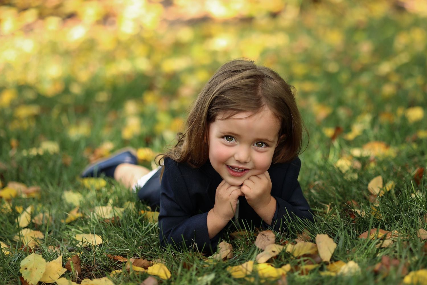 Upsherin boy leaning on his hands in the grass surronded by yellow leavs