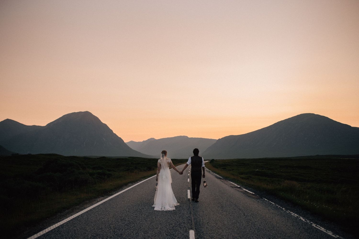 A windswept couple in wedding attire walking along a misty beach.