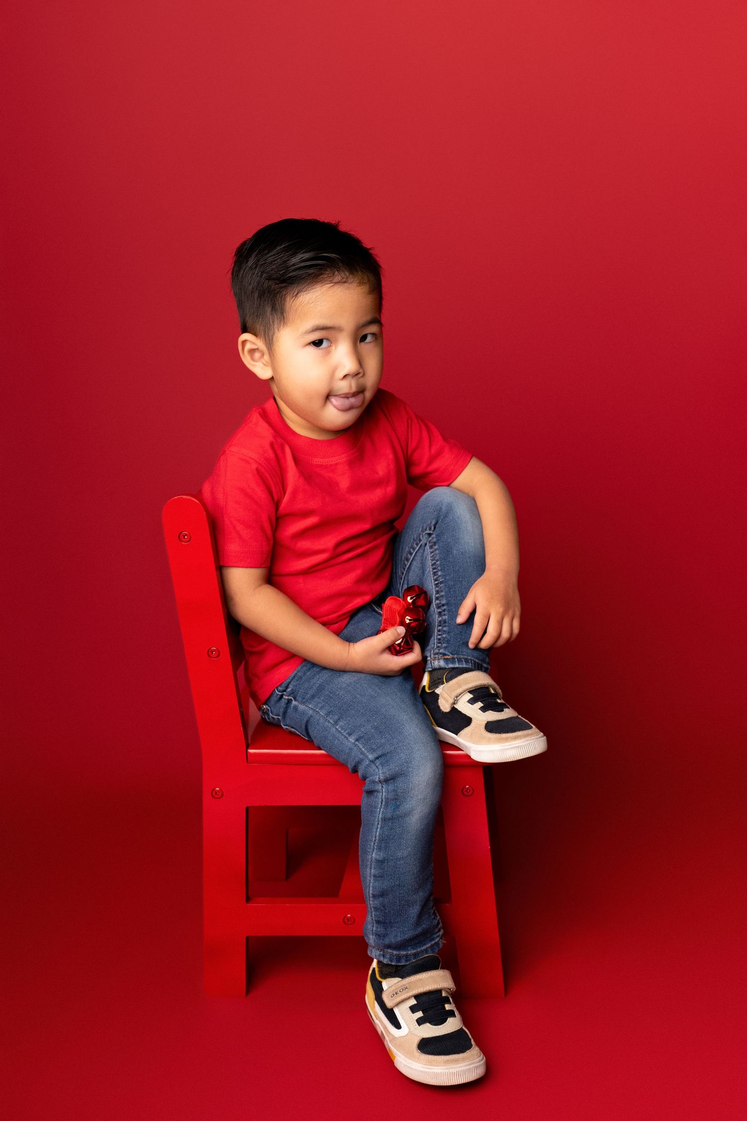 Child in red shirt and jeans sitting on red chair against vibrant background.