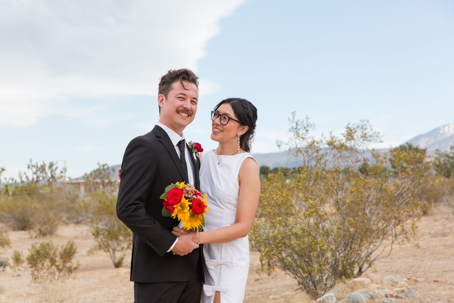 Wedding couple sharing intimate moments in a desert landscape with mountains in background.