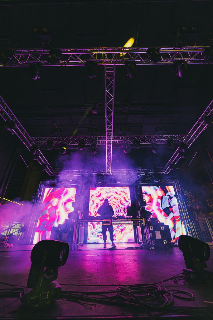 Concert stage with LED video wall displaying pink visuals and purple atmospheric lighting.
