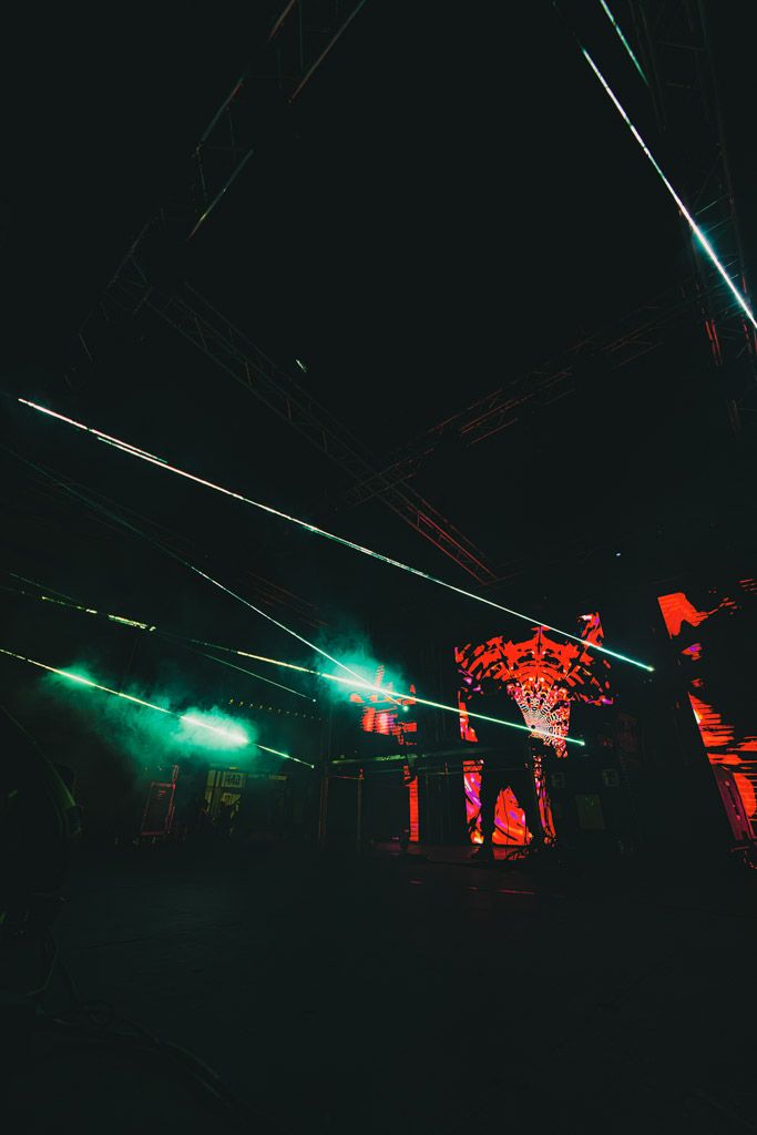 Dramatic light show with green and red laser beams cutting through darkness during an outdoor nighttime performance.
