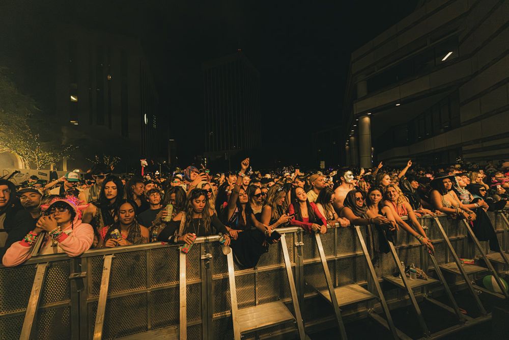 Concert crowd silhouettes raise their hands in excitement during a live performance with dramatic lighting.
