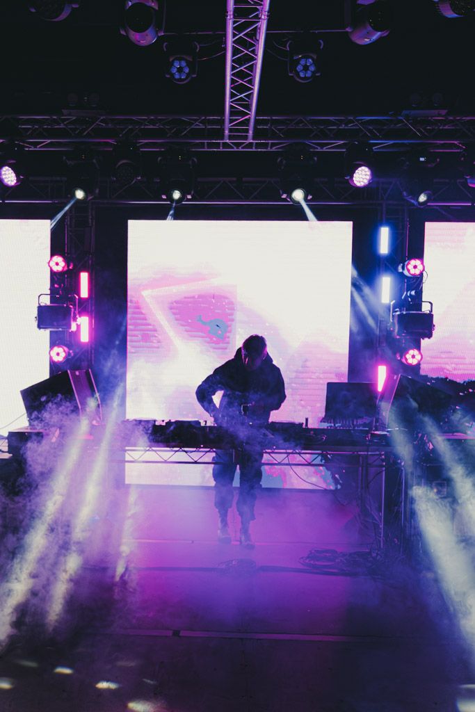 Stage performers silhouetted against vibrant purple lighting and fog during a show.