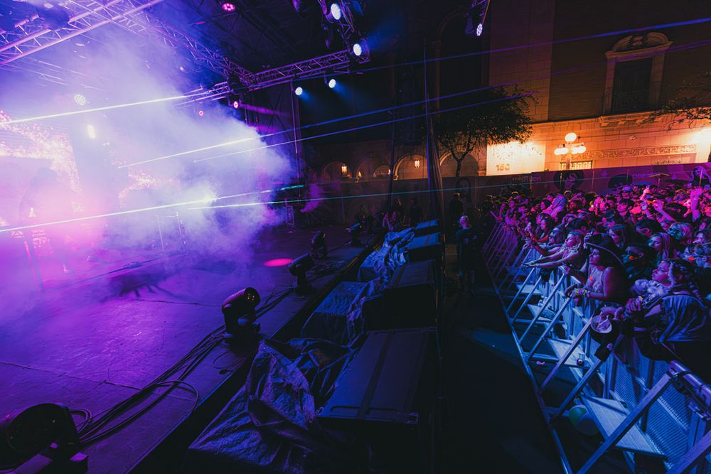 A concert venue bathed in purple and blue lighting with fog effects creating an atmospheric nightclub ambiance.