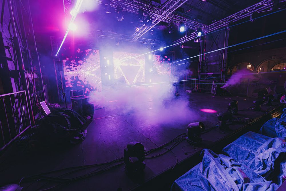 Concert stage illuminated with vibrant purple lighting and fog effects creating an atmospheric performance environment.