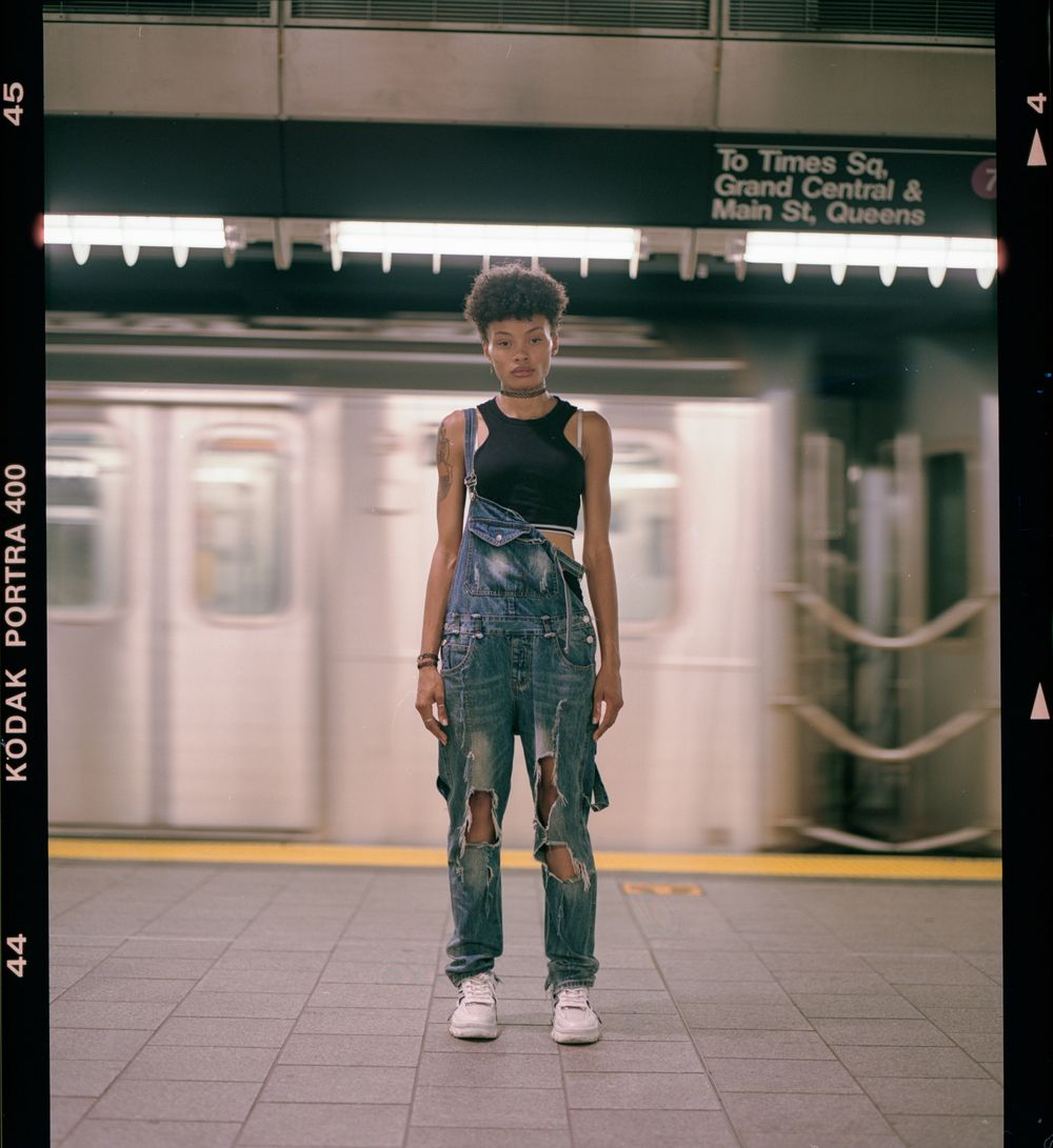 Person in overalls standing on subway platform in urban setting.