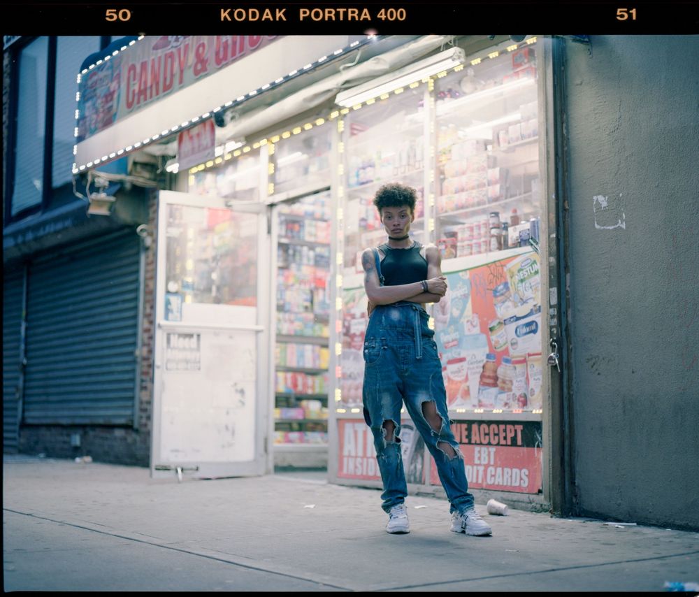 Person in denim overalls standing outside candy store with illuminated storefront.