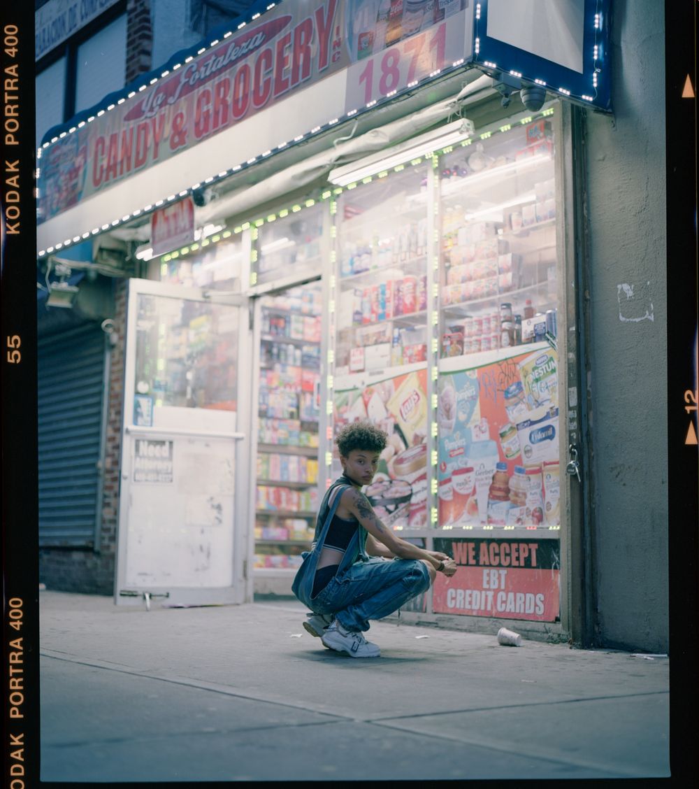 Person crouching outside illuminated candy store at night.