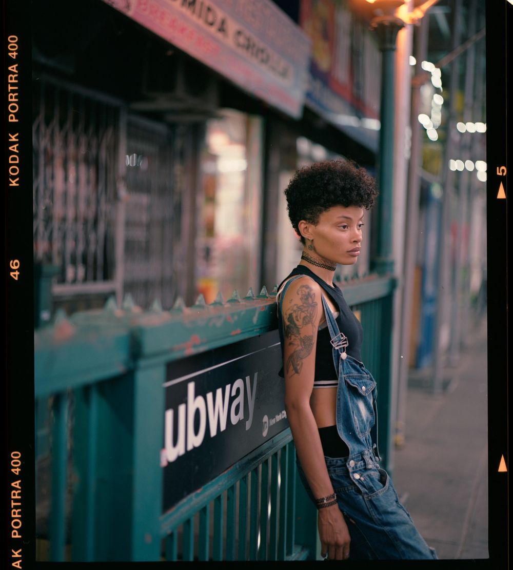 Person in casual wear standing near subway entrance at dusk.