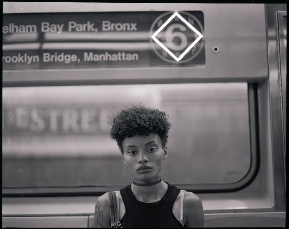 Black and white portrait shot inside subway car with destination sign visible.