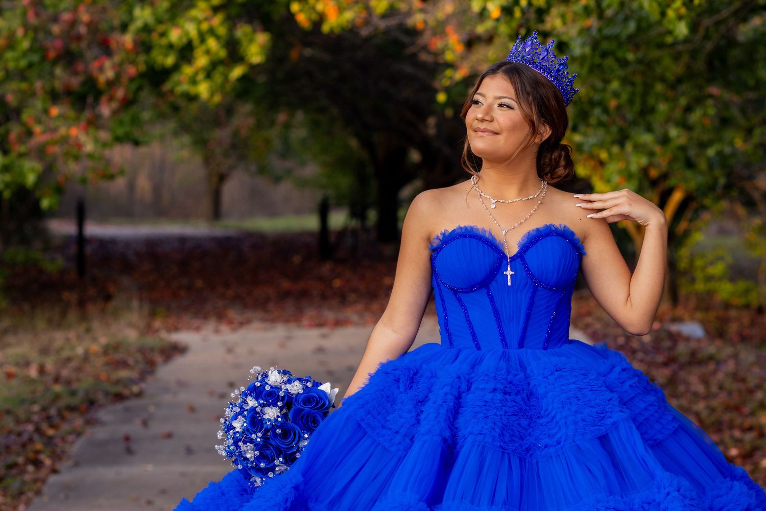 A bride in a vibrant royal blue ball gown poses elegantly among autumn foliage in an outdoor setting.