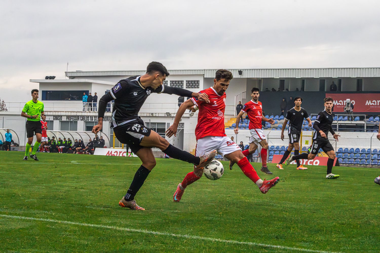 Soccer players from opposing teams dive and stretch for the ball during an intense play.