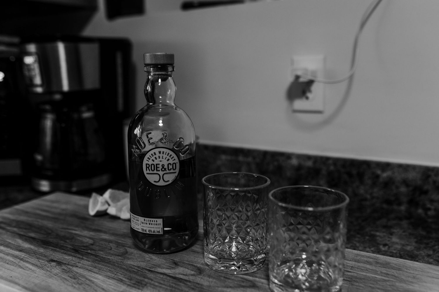 Black and white photograph of vintage glass bottles and barware arranged on a dark surface with moody lighting.