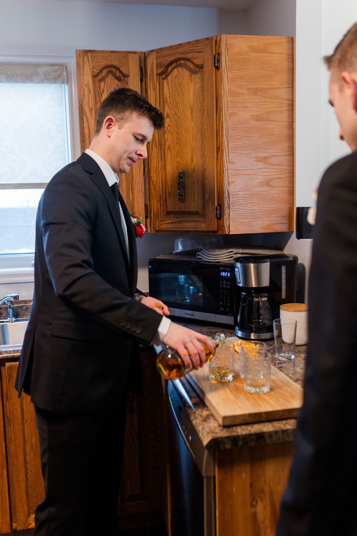A person in a suit prepares food in a kitchen with wooden cabinets.