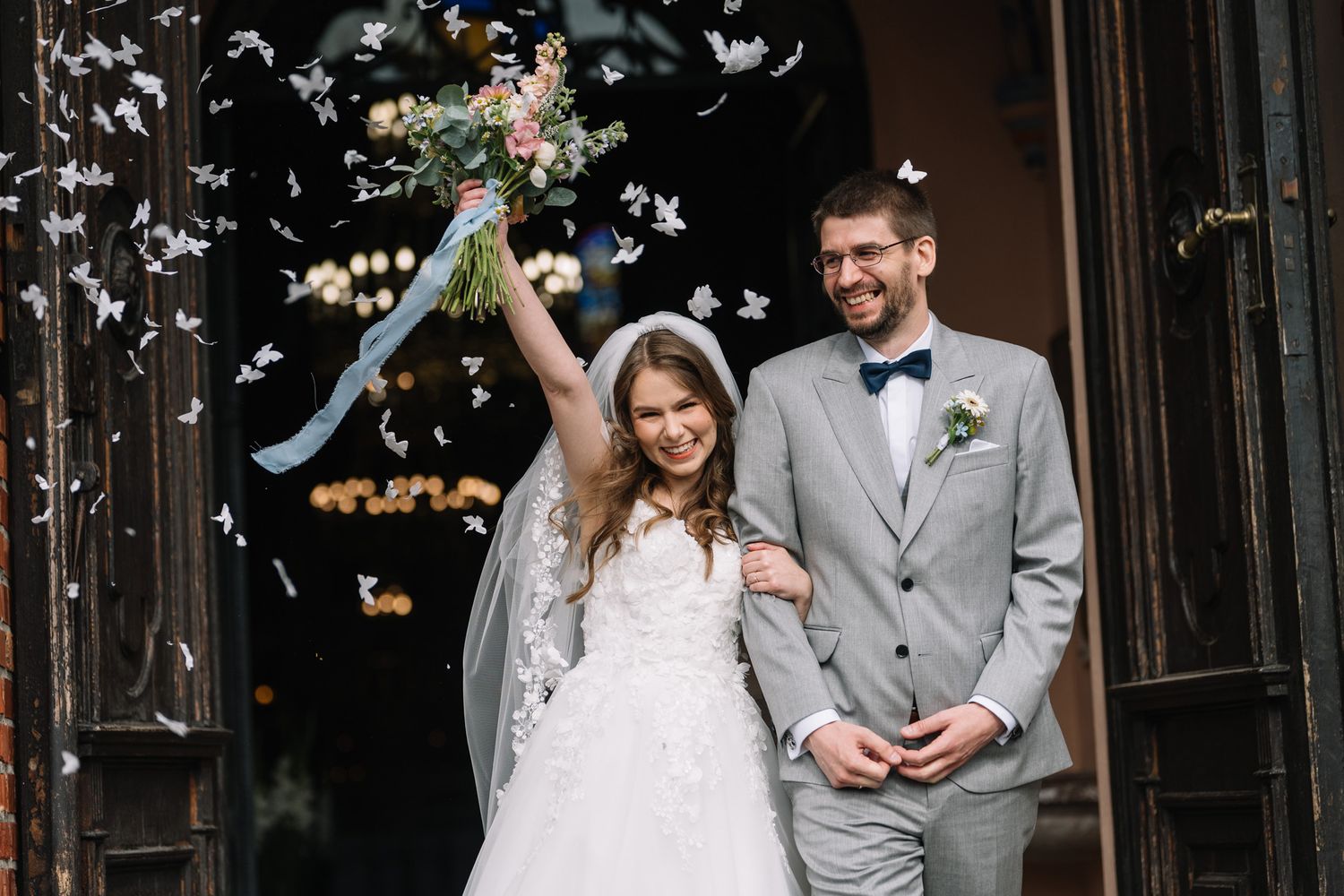 Newlyweds exit their wedding ceremony as guests shower them with white flower petals in joyful celebration.
