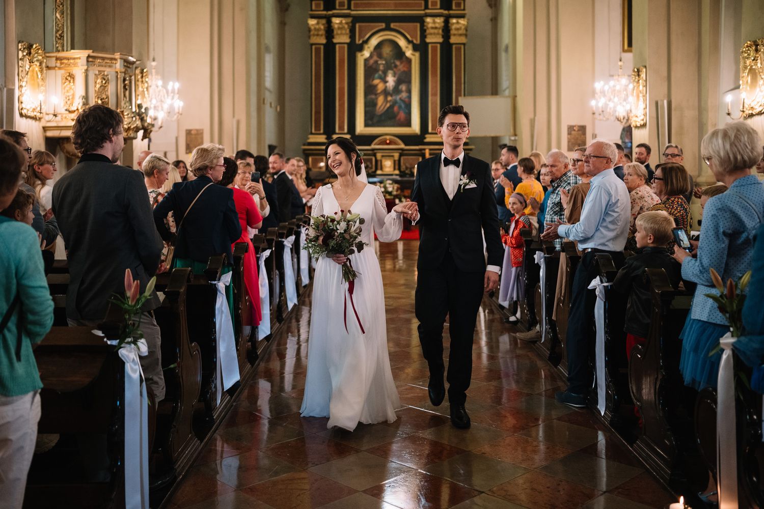 Wedding guests mingle and dance in an elegant ballroom with crystal chandeliers and ornate decor.