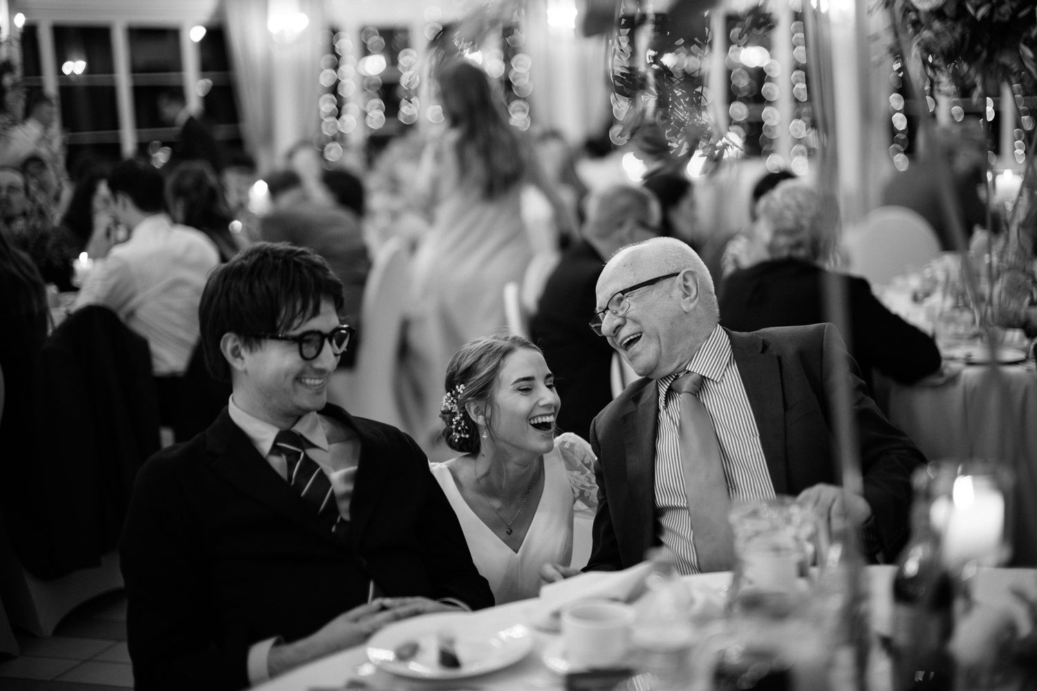Black and white photo of wedding guests laughing and celebrating on a crowded dance floor.