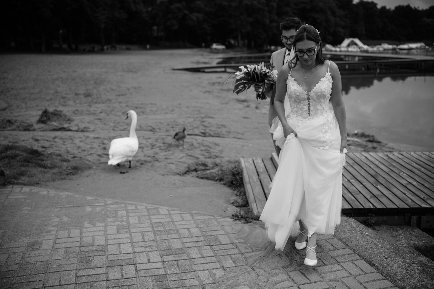 A series of black and white photos showing a bride in a white dress walking along a path near water with geese.