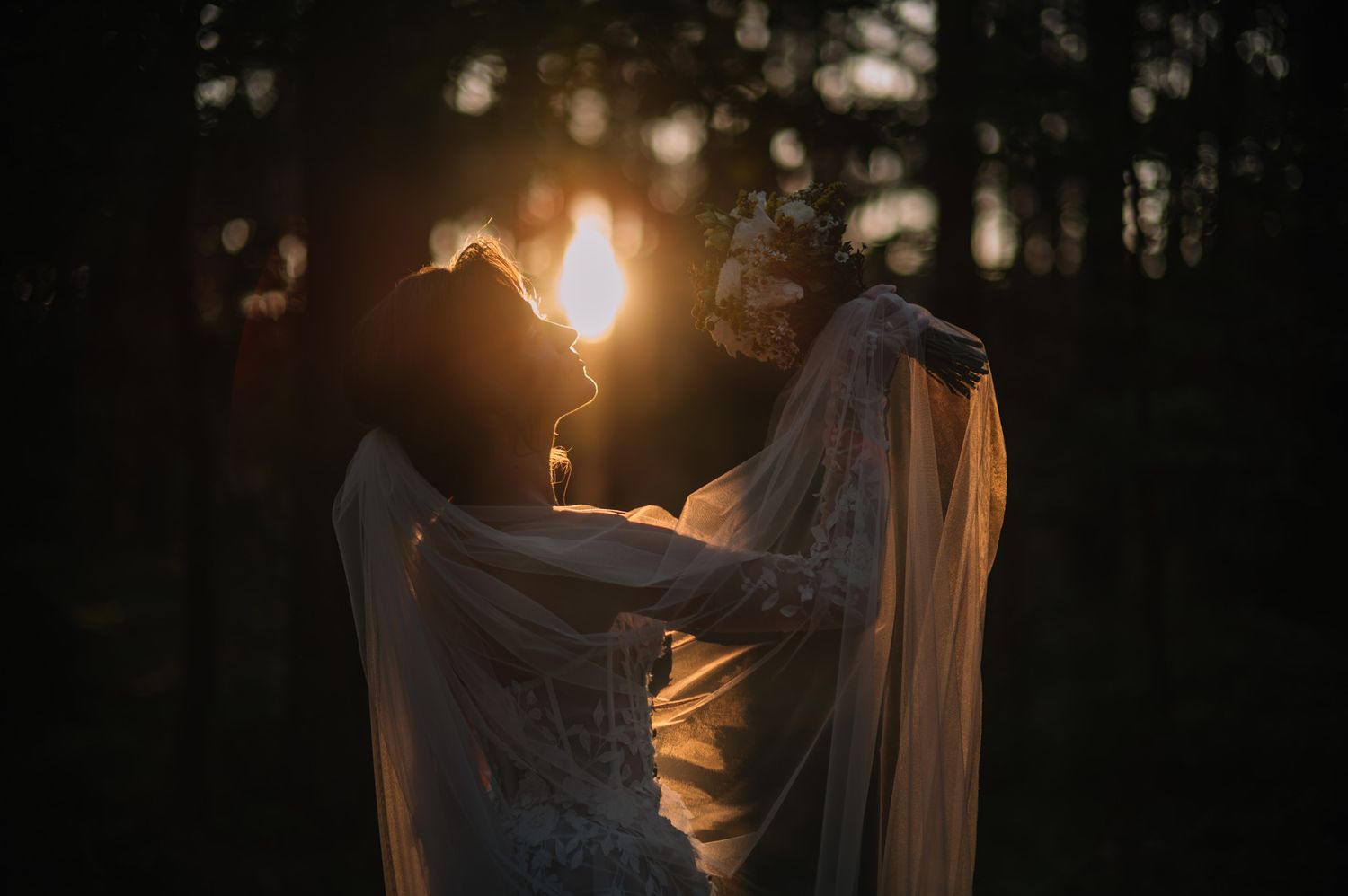 Silhouetted couple embraces at sunset creating a romantic backlit scene with a flowing veil.