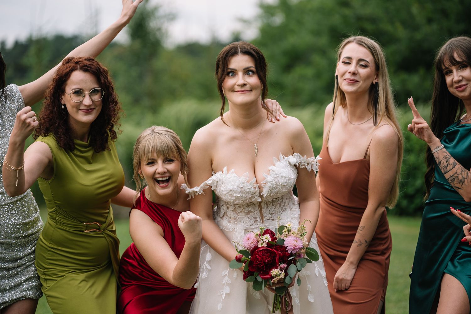 A group in colorful dresses and formal attire poses together outdoors during a wedding celebration.