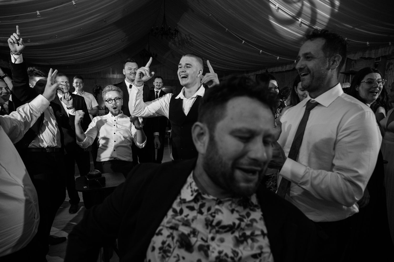 Wedding guests dance and celebrate on a crowded dance floor at an evening reception party.