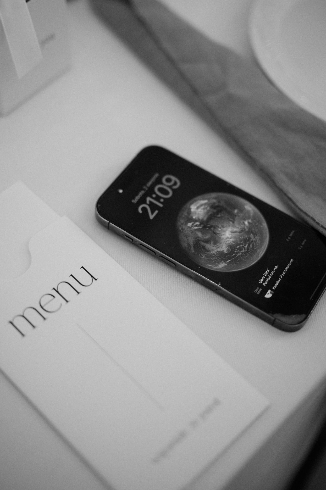 Black iPhone displaying moon phase app on white surface in minimalist monochrome composition.