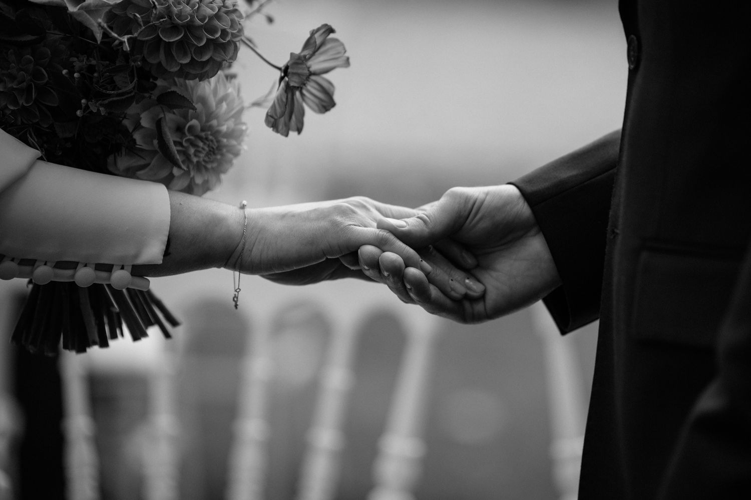 Black and white close-up photo of hands passing a white paper between them in a dark setting.