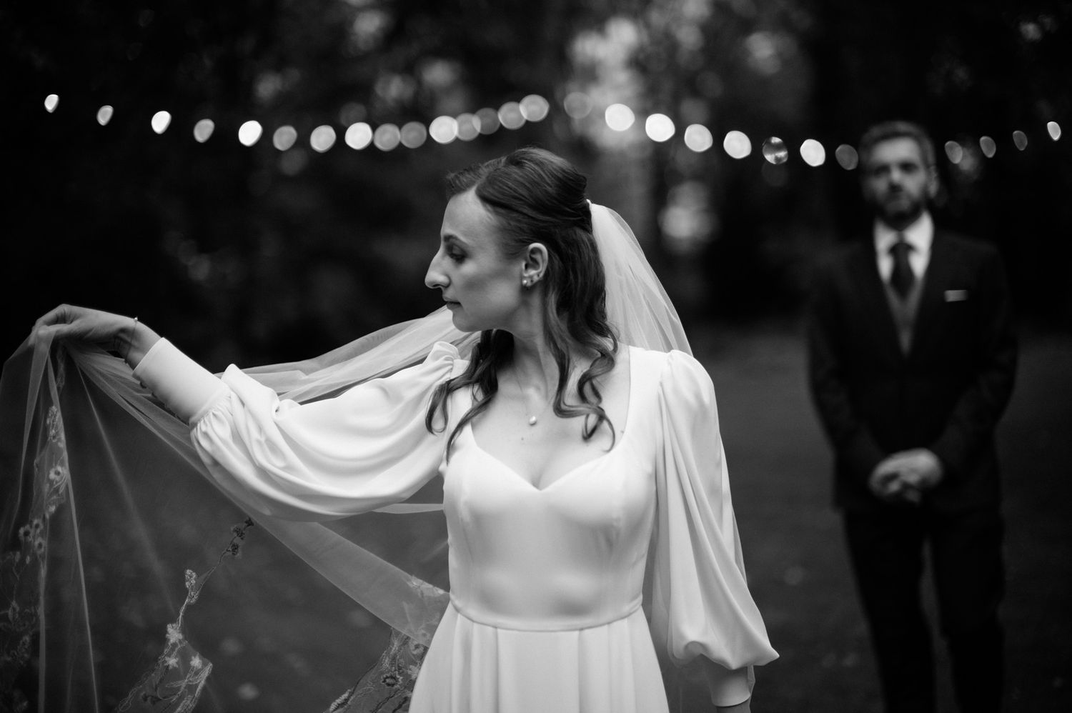 A bride and groom share their first dance under romantic string lights at an outdoor evening wedding reception.