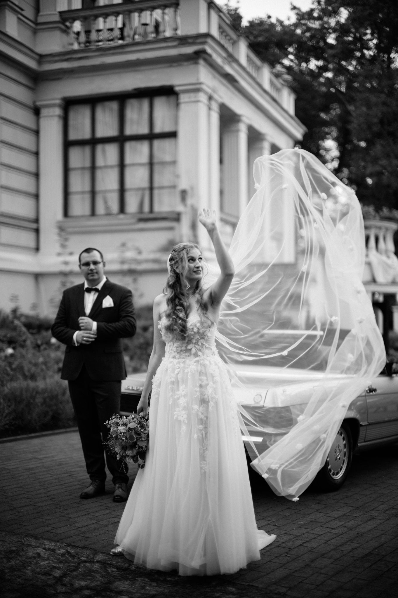 A flowing bridal veil catches the wind in a series of romantic black and white photos outside a stately building.