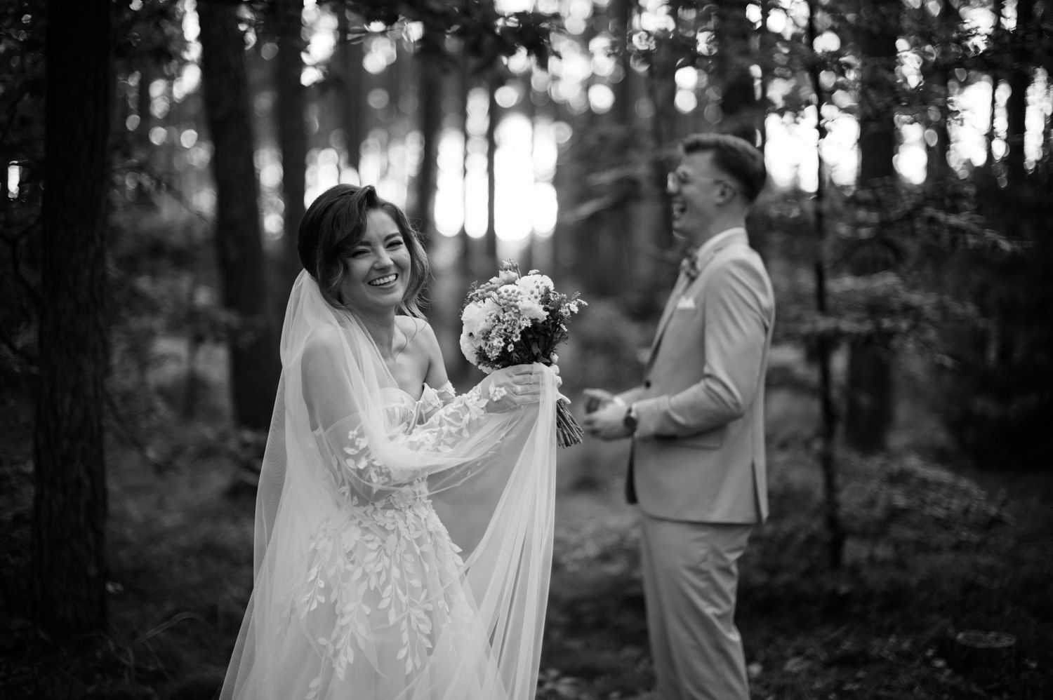 A bride and groom share a romantic moment in a sunlit forest setting during their outdoor wedding ceremony.