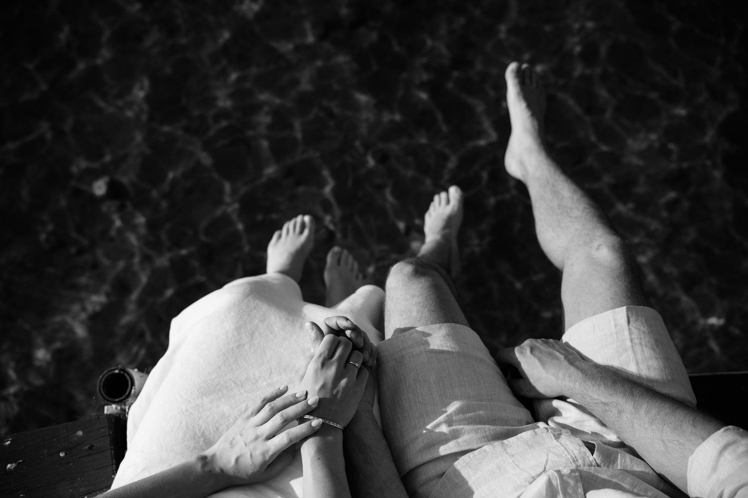Black and white artistic photograph of nude figures reclining against dark textured background.
