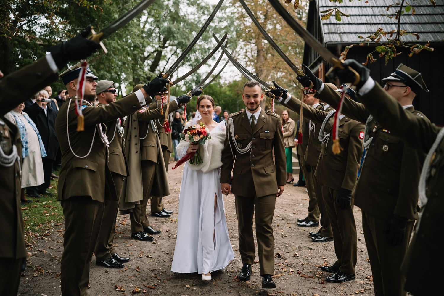 Wedding party walks through a tree-lined path as guests form an aisle and shower them with confetti.