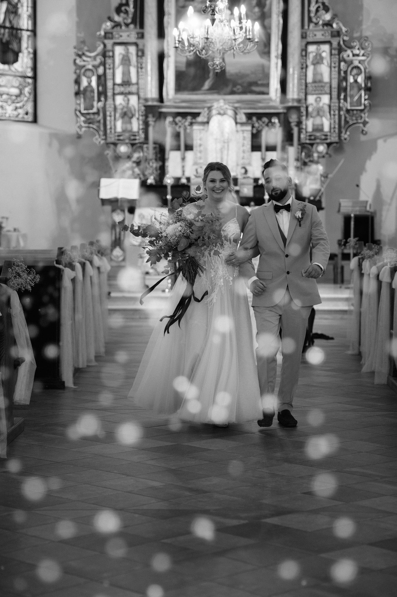 A series of black and white wedding ceremony photos showing movement down a church aisle with bokeh effects.