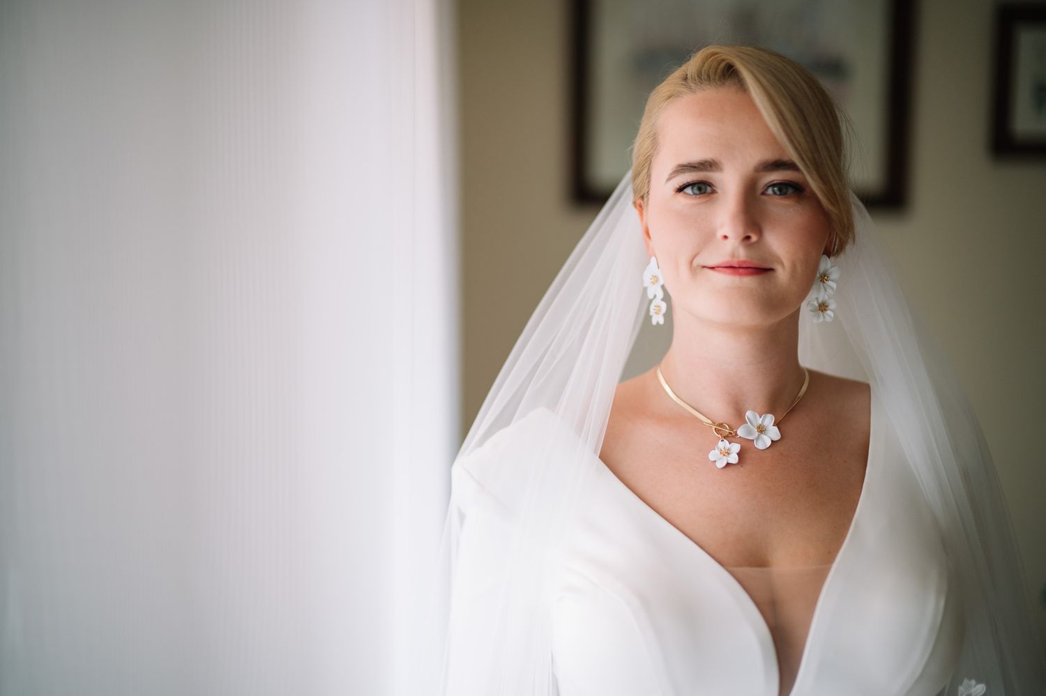 A bride wearing a white veil and pearl necklace poses for a bridal portrait in soft natural light.
