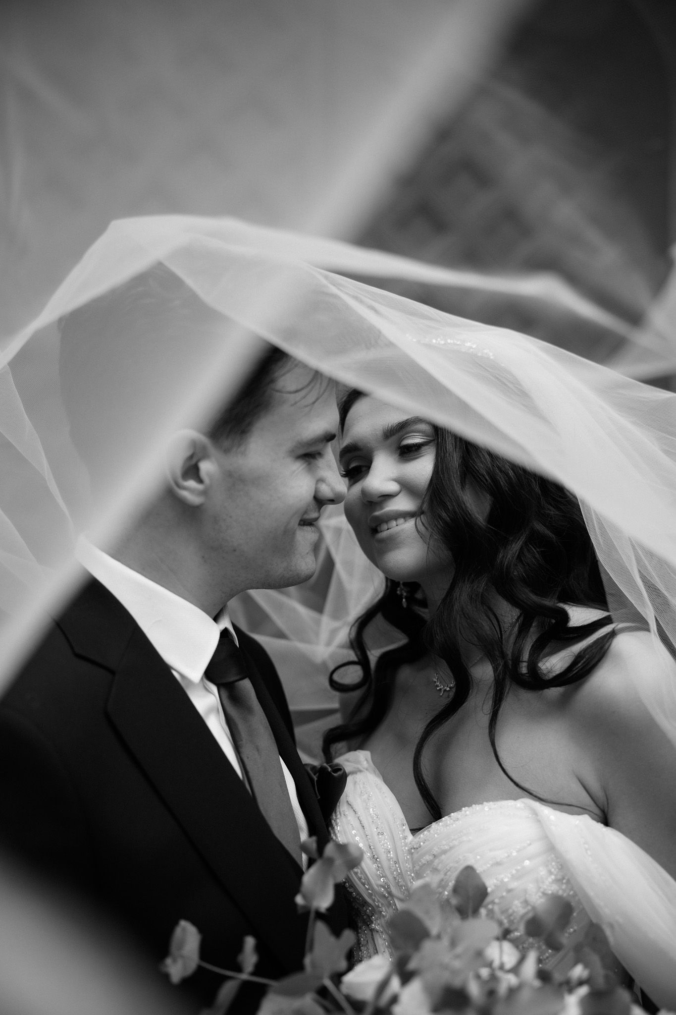 A romantic black and white wedding photo series showing tender moments between a couple under a flowing veil.