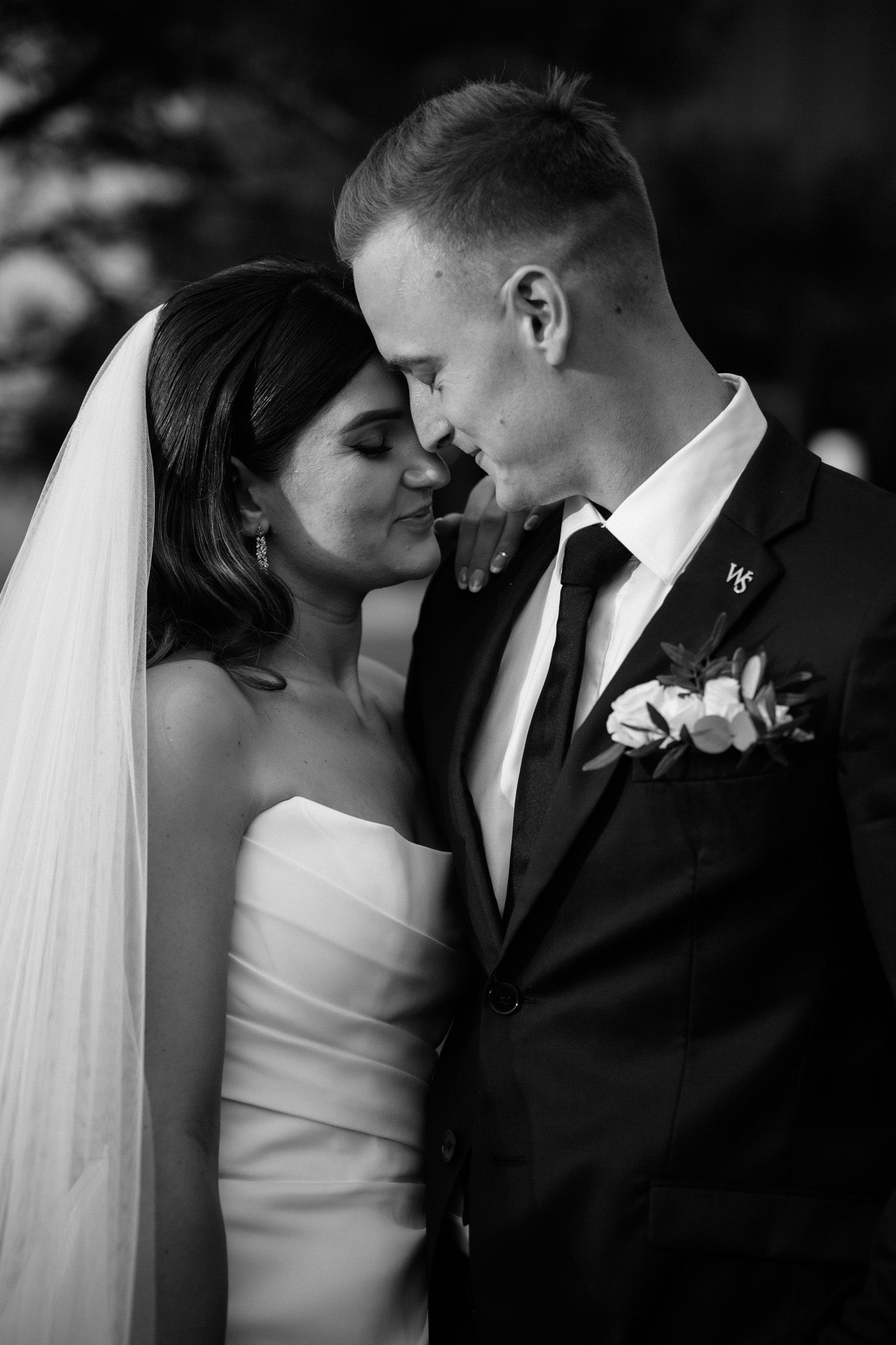 A romantic black and white wedding portrait showing a tender moment between newlyweds with the bride in white and groom in suit.