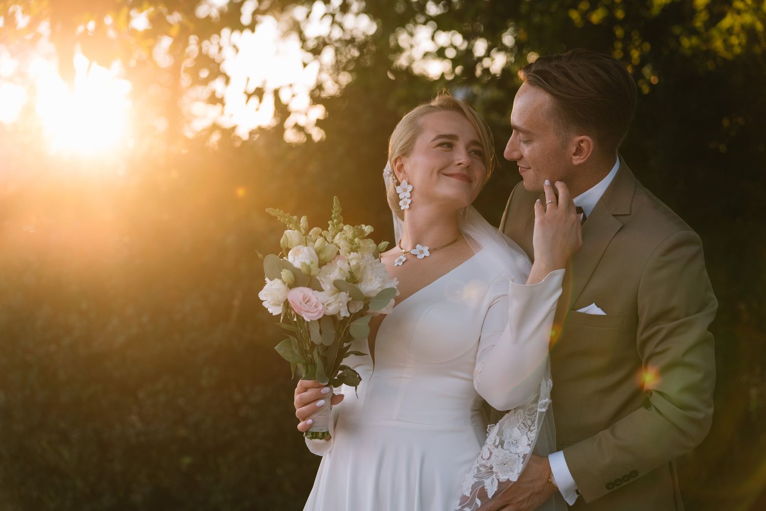 A couple shares a tender moment during their wedding photoshoot at sunset in a garden setting.