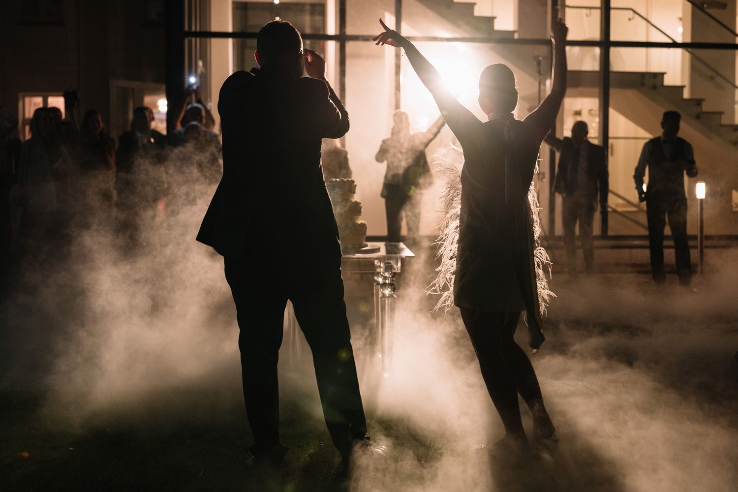 Silhouetted figures dance in atmospheric fog at a dimly lit indoor venue.