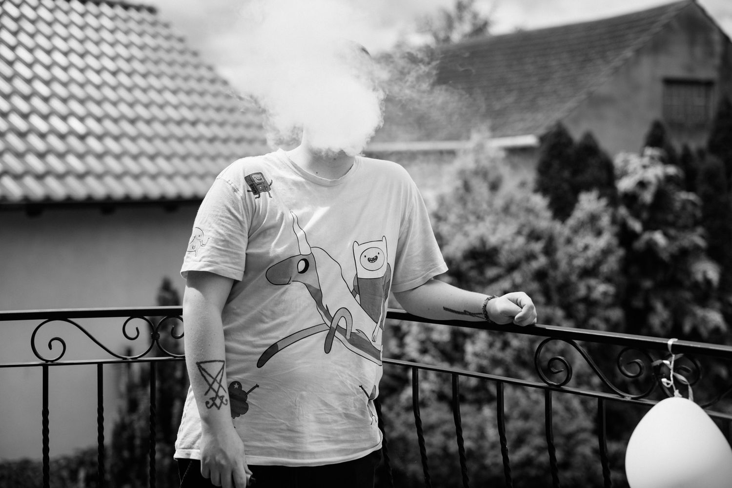 A person in a white t-shirt and shorts stands on a balcony overlooking a garden area.
