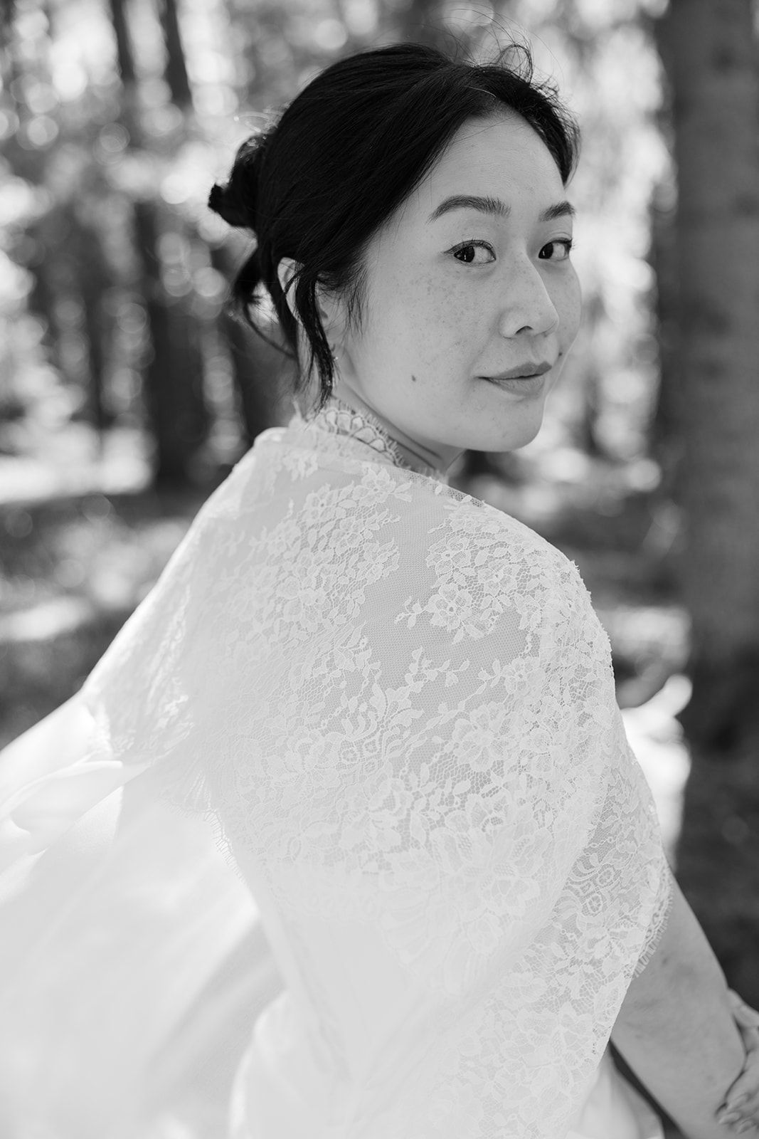 Black and white portrait of someone in delicate white lace looking over their shoulder in a natural outdoor setting.