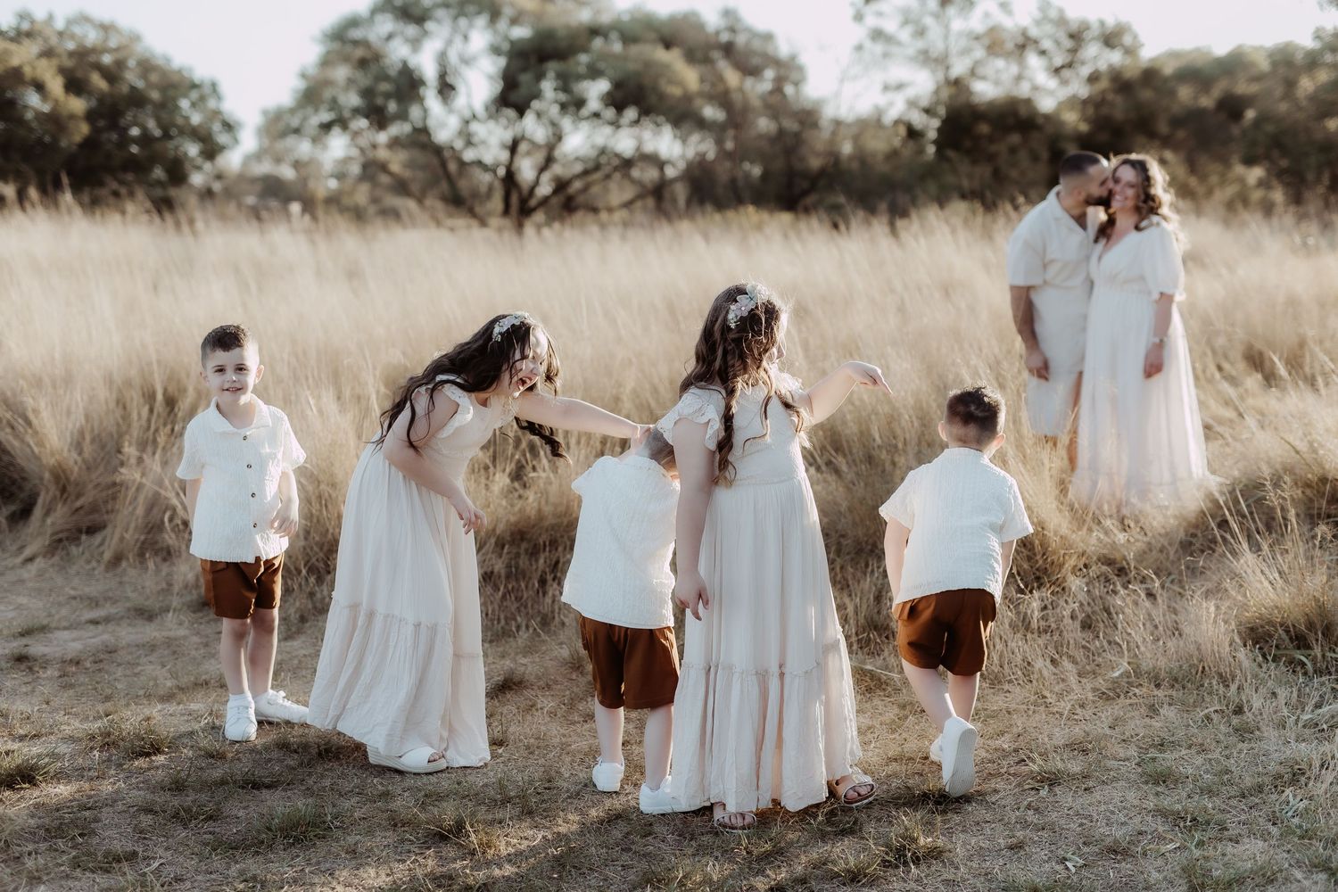Family walking together through a sunlit field wearing coordinated white and neutral outfits.