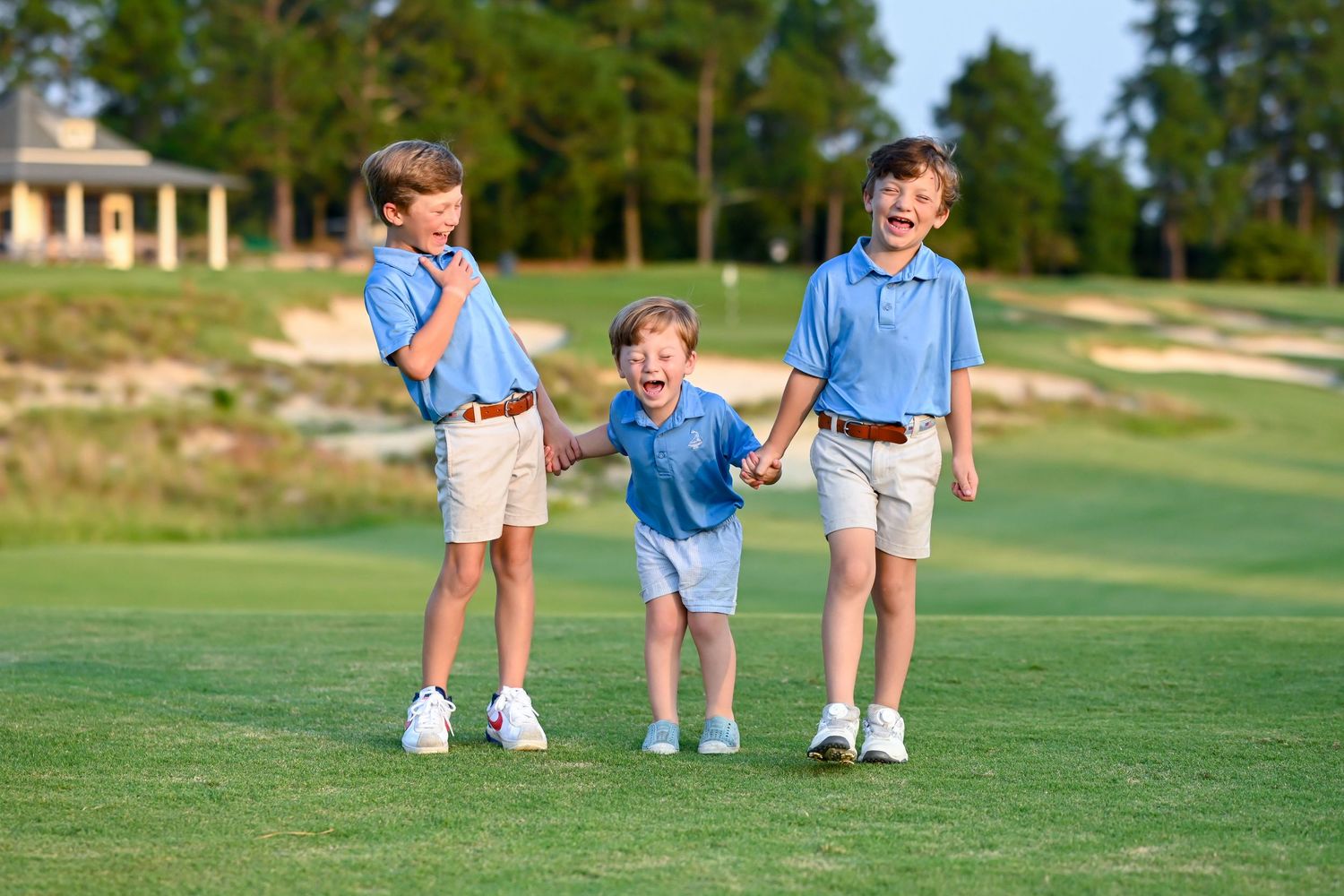 Children walking together on a sunny golf course wearing coordinated blue and white outfits.