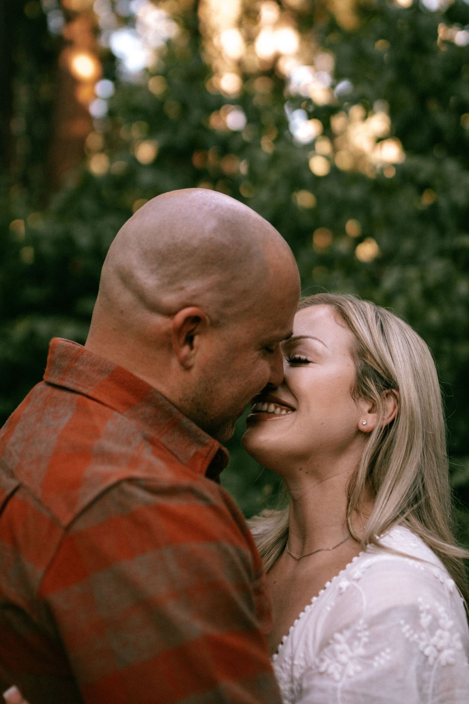 A couple shares tender moments in a romantic outdoor photoshoot with sunlit trees in the background.