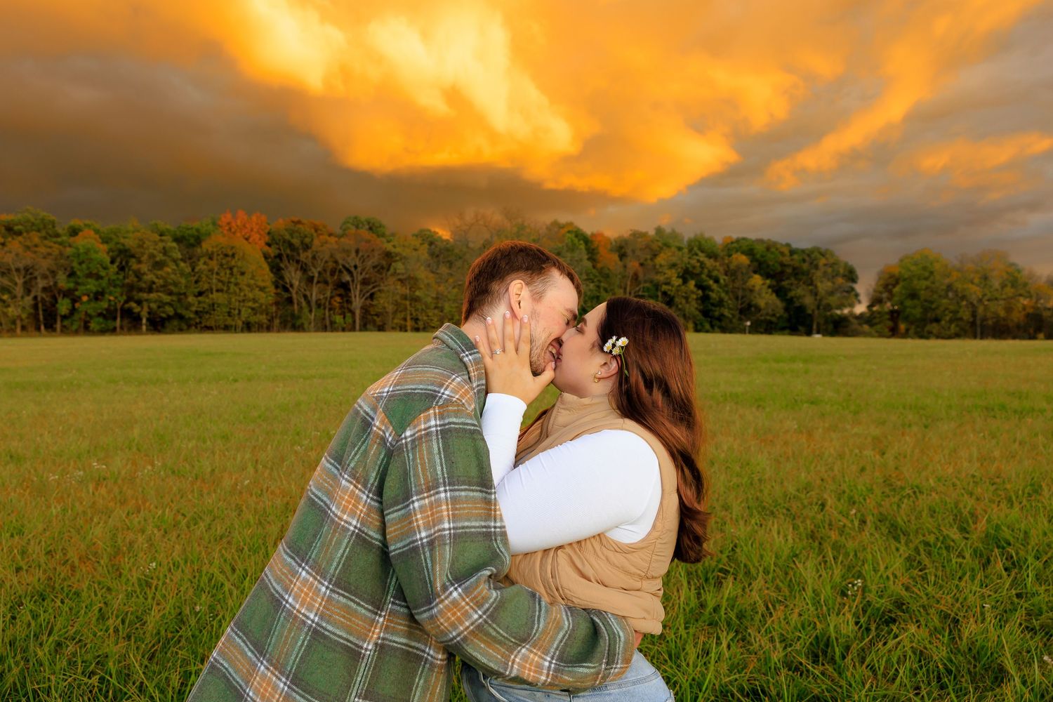 A couple walks through a scenic autumn field during golden hour with warm sunlight and rolling hills in the background.