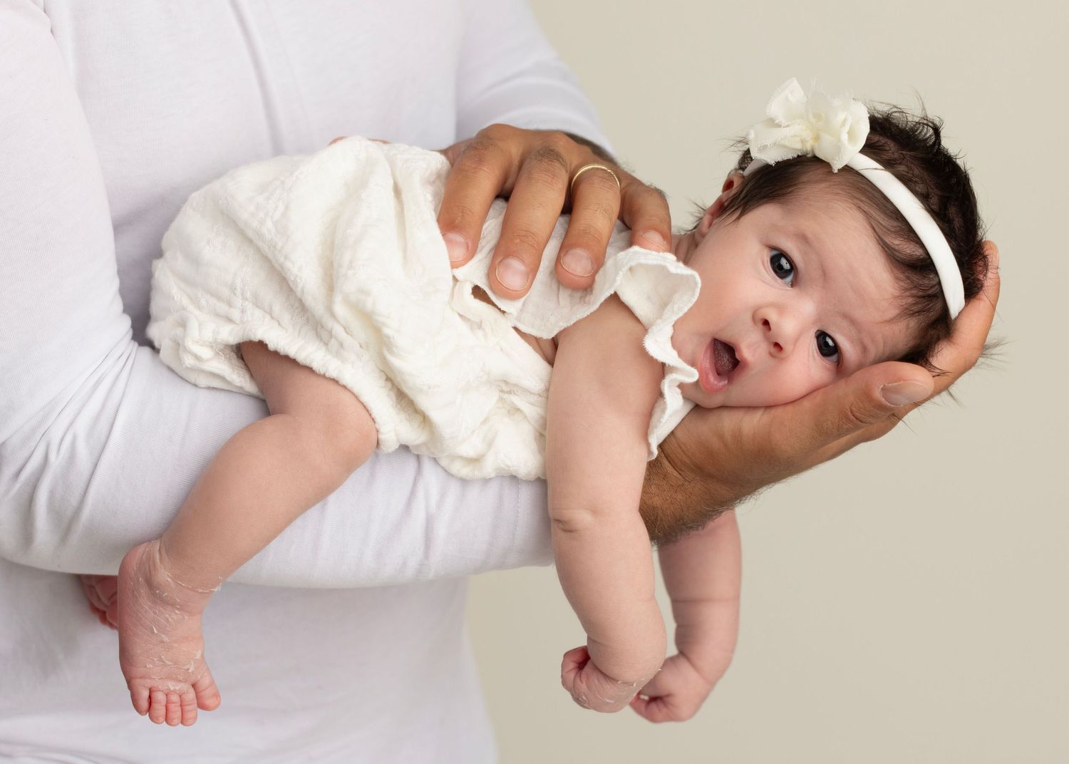 Adorable baby in white clothing lies on a white blanket in a series of connected photos showing different poses.