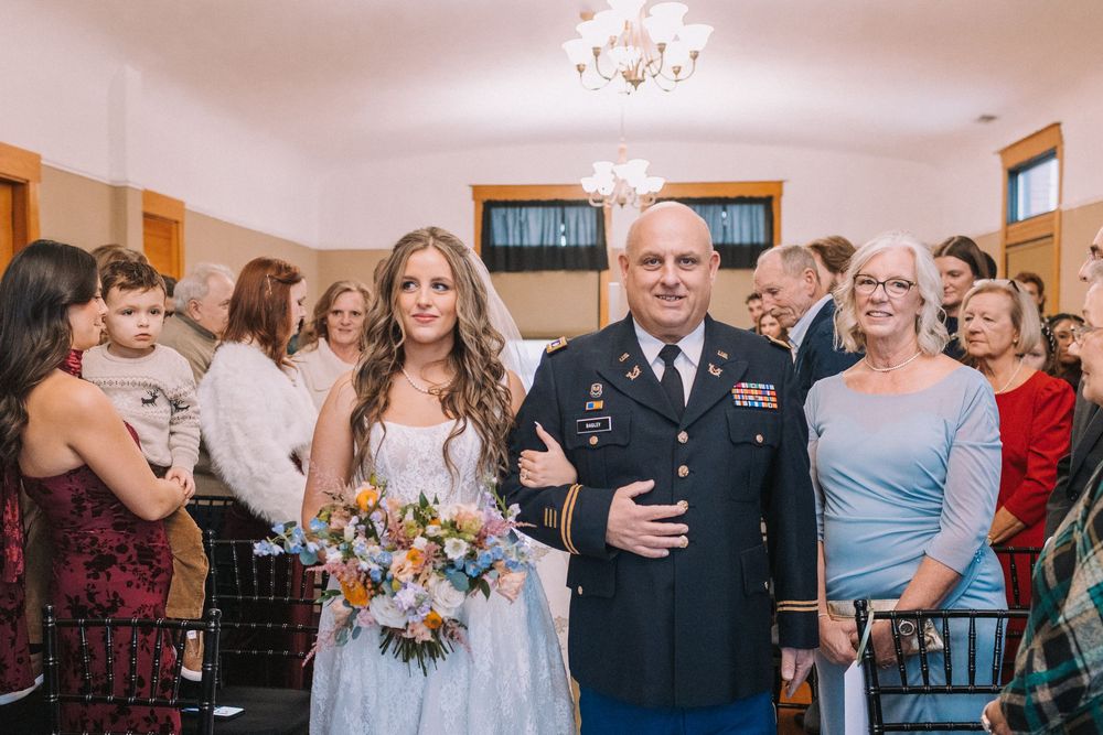 Wedding ceremony in progress with bridal party and military groom in uniform.