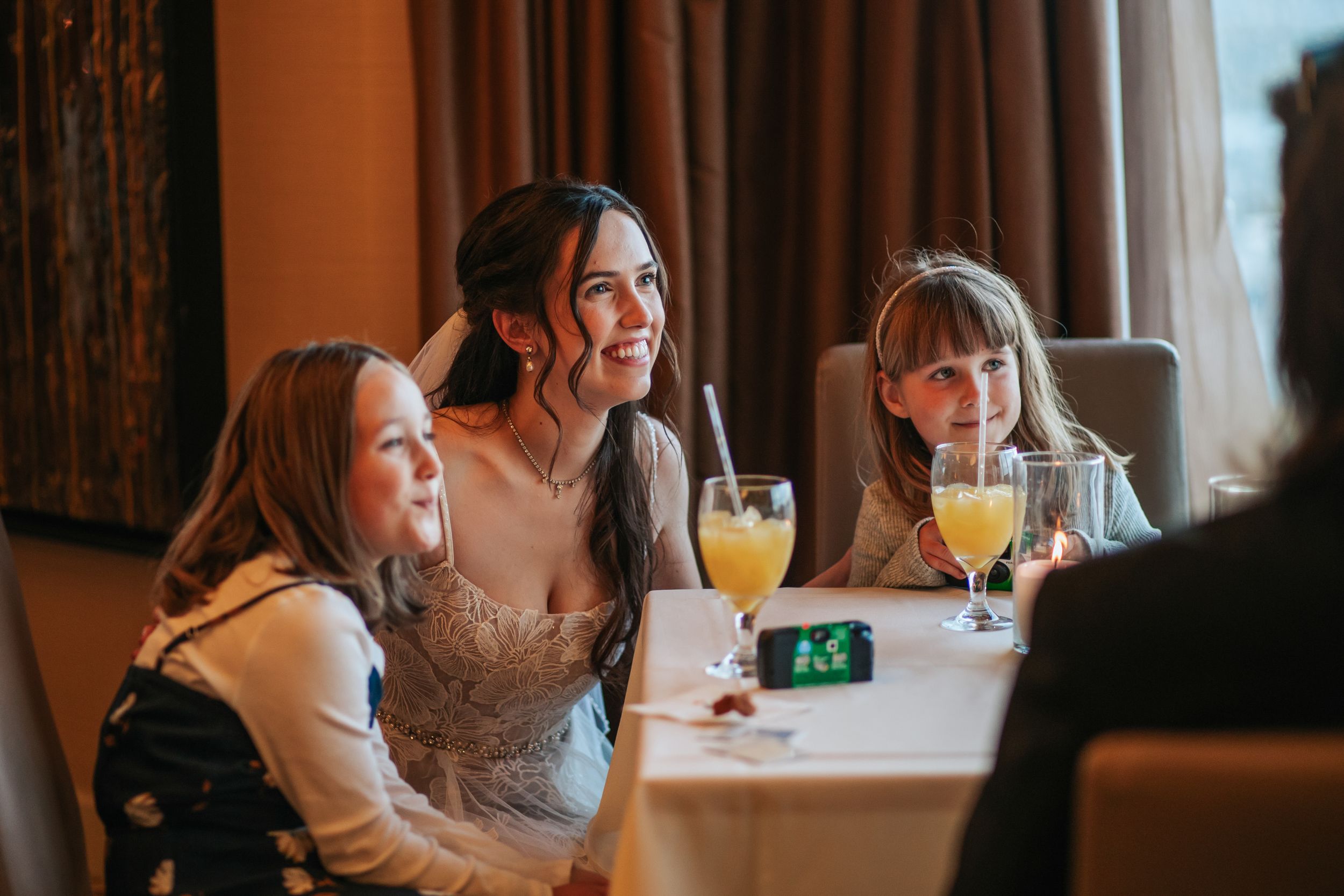 Three friends share drinks and laughter while sitting at a restaurant table with orange juice cocktails.